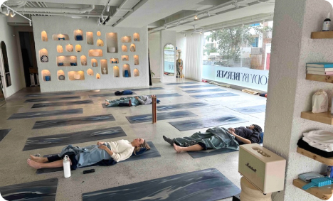 People lying on yoga mats in a bright studio, covered with blankets, during relaxation.