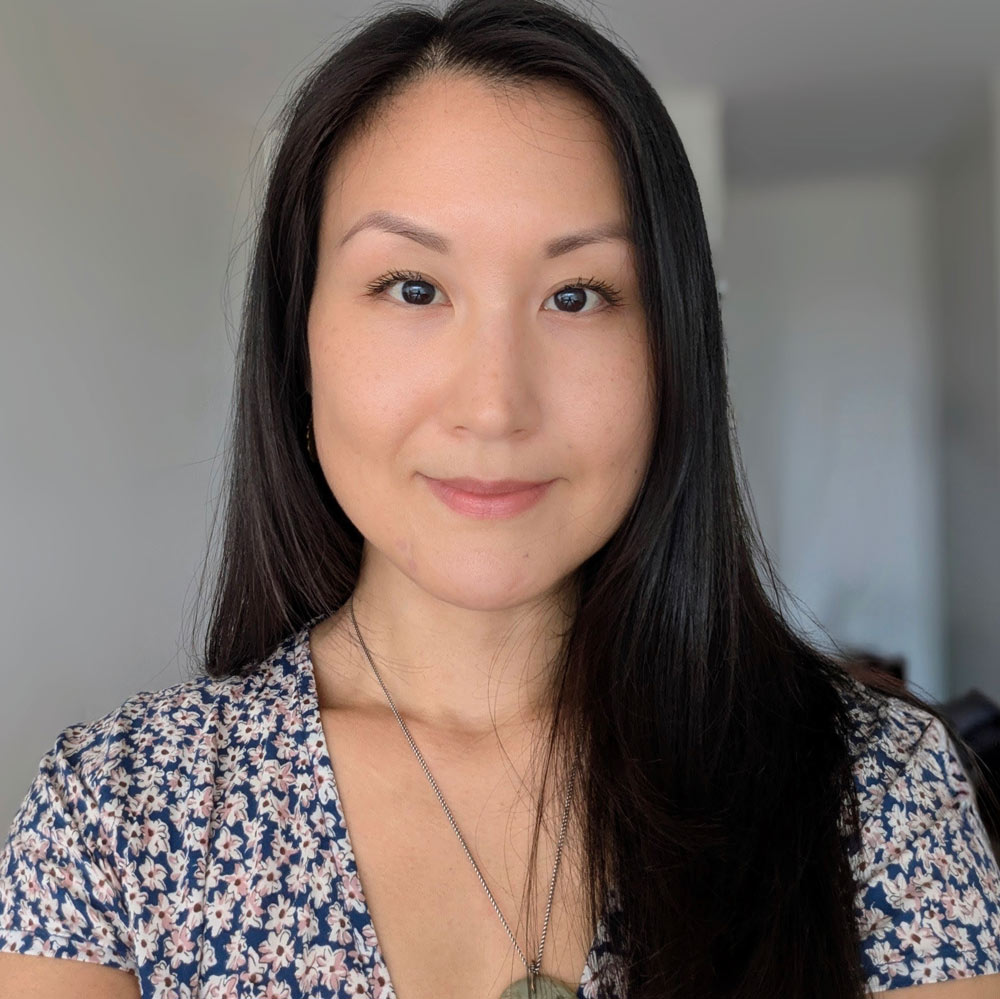 Our Team: Woman with long dark hair in a floral top, facing the camera and smiling slightly.