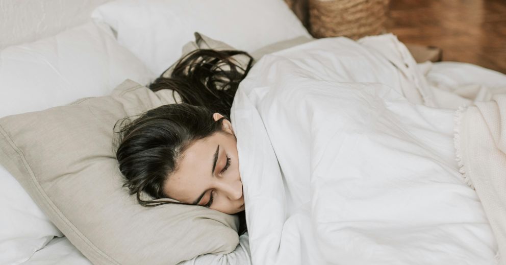 Woman sleeping in bed under a white blanket, ready to reset your sleep naturally.