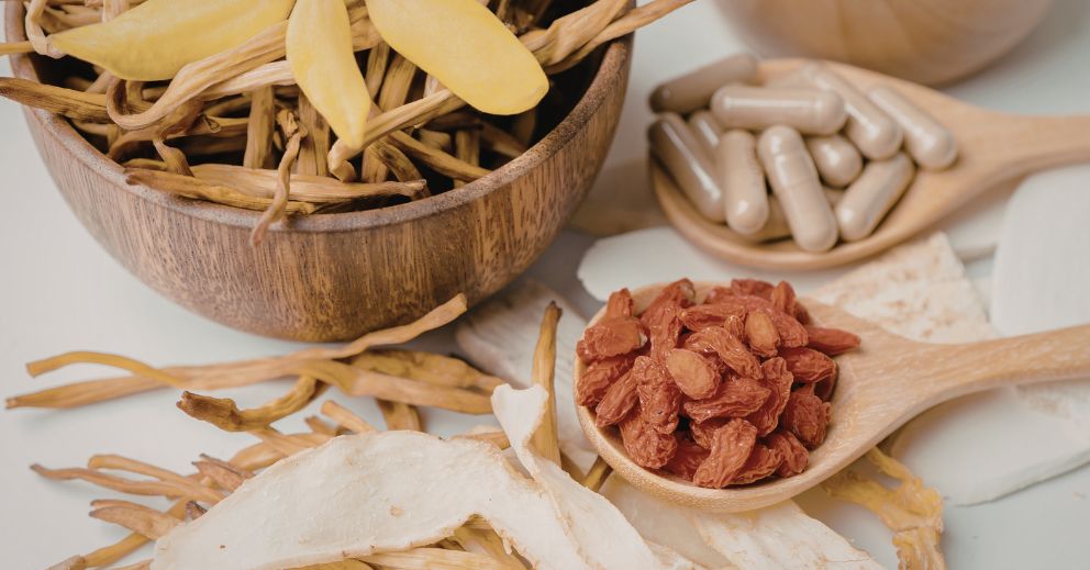 Wooden bowls and spoons with dried herbs, red berries, white slices, capsules—Chinese medicine.
